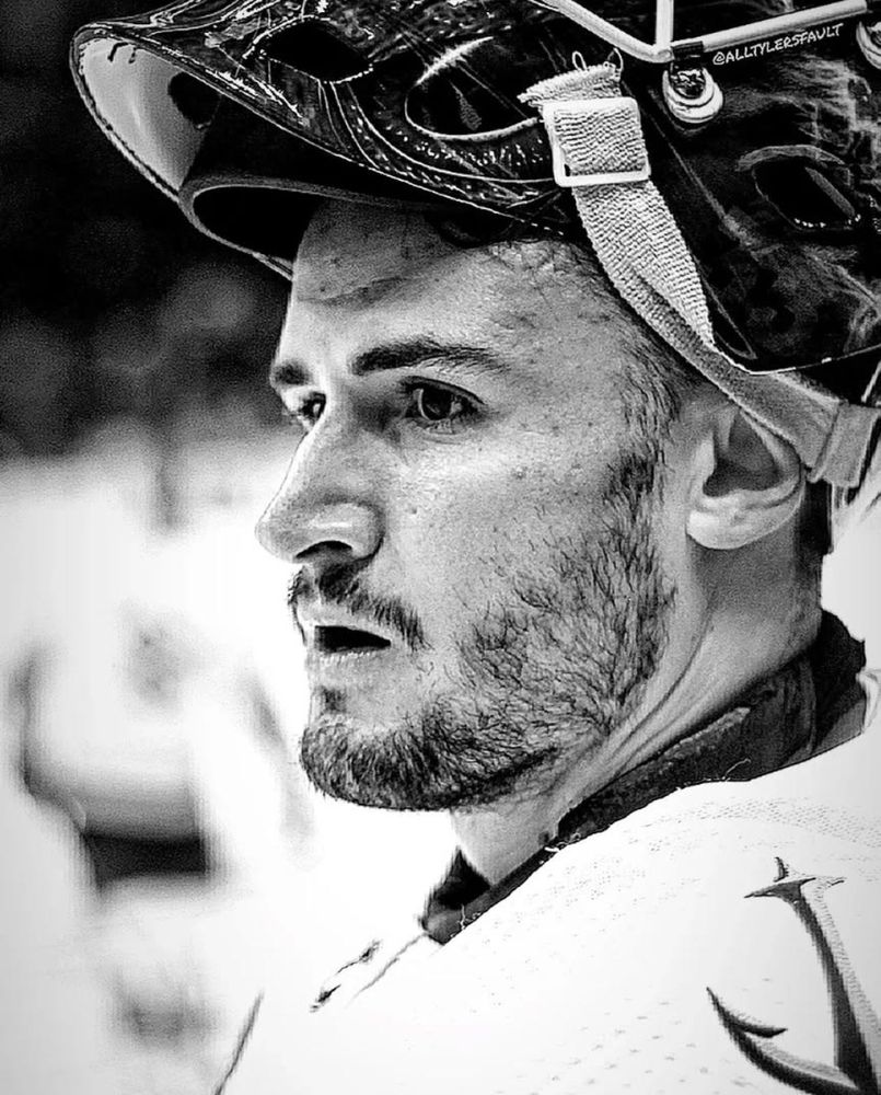 Black and white side profile of Seattle Kraken goaltender Joey Daccord. Goalie mask is in the upright position and Dax's mouth is agape as if in awe.