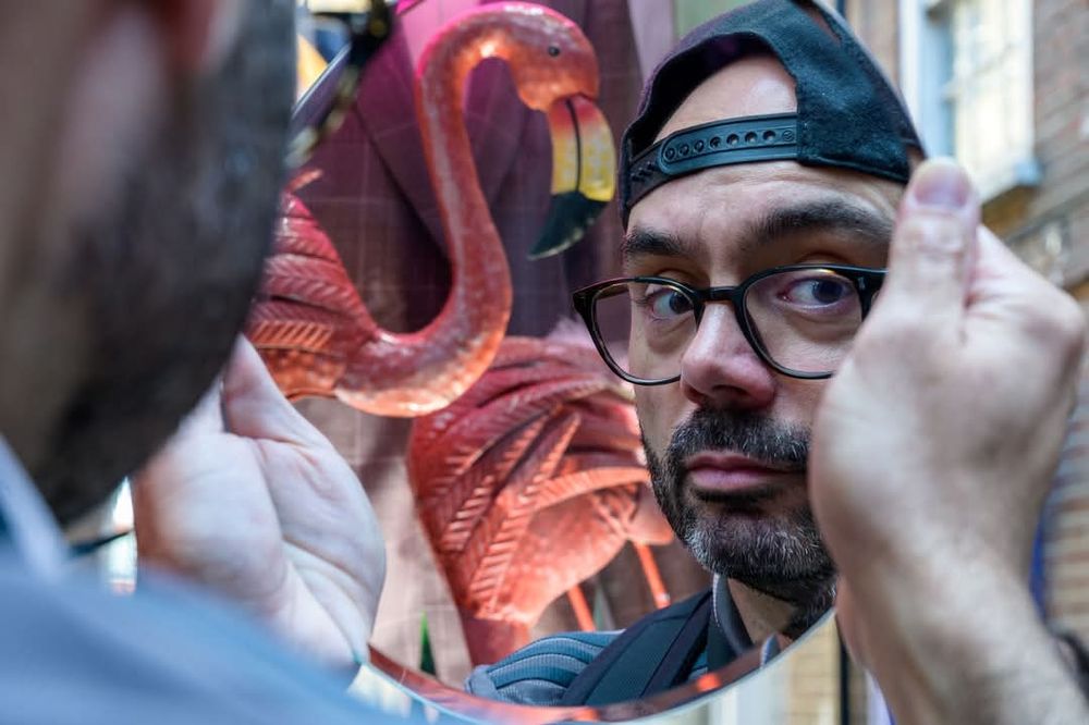 Mirror with reflection of a bearded man with cap and glasses with a flaming behind him. 