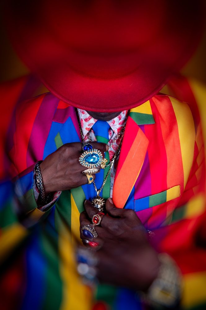 Portrait of a man wearing a vivid rainbow-striped suit with bold colours across the jacket and shirt. His confident expression and the dynamic pattern of his outfit create a striking and joyful visual statement.