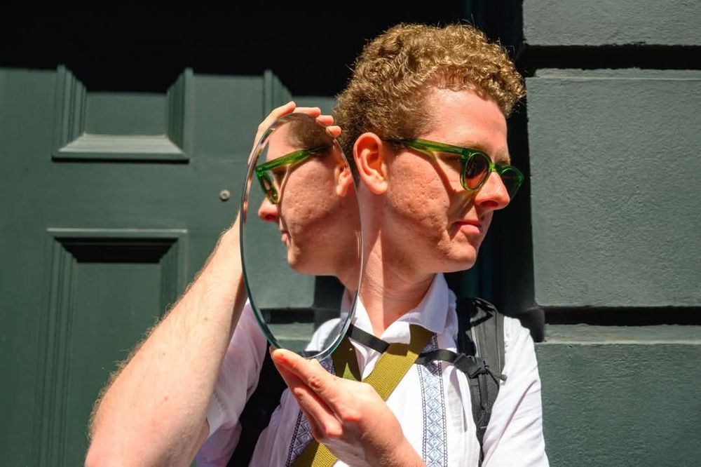 Mirror with reflection of a red-head man against a green background.