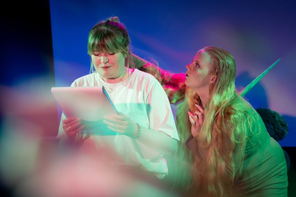 Blonde women in costume performing on stage in SNOLIGOSTER. Theatrical lighting and surreal in-camera effects create a dreamlike, satirical atmosphere. All images captured live using a Reflect Lens filter.