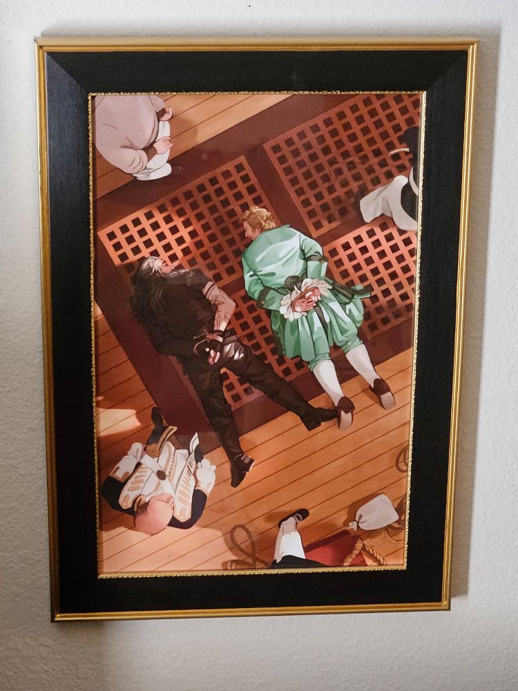 A framed print of the OFMD foot touch scene from E1S8 by Ashokanspring. It is a top-down view of Ed and Stede face down on the deck of the Revenge, their hands bound behind their backs. Chauncey Badminton stands just to the left of Ed. Ed is in his black leathers and Stede is wearing his turquoise silk suit. They are looking directly into one another's eyes. Ed is reaching out with one leg to touch Stede's foot. Lindsey Buckingham is about to kick into his outro guitar solo.