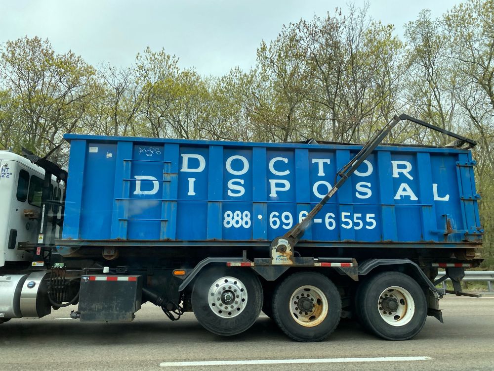 A big blue garbage truck with white letters spelling out “DOCTOR DISPOSAL”