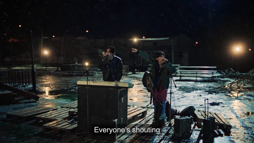 Scene from the “CINEMA” music video

Lee Know and Seungmin performing to an empty crowd. Lee Know is standing in front of a keyboard, and Seungmin is playing the guitar. It’s dark outside with a few lamp posts, and the lot looks abandoned.