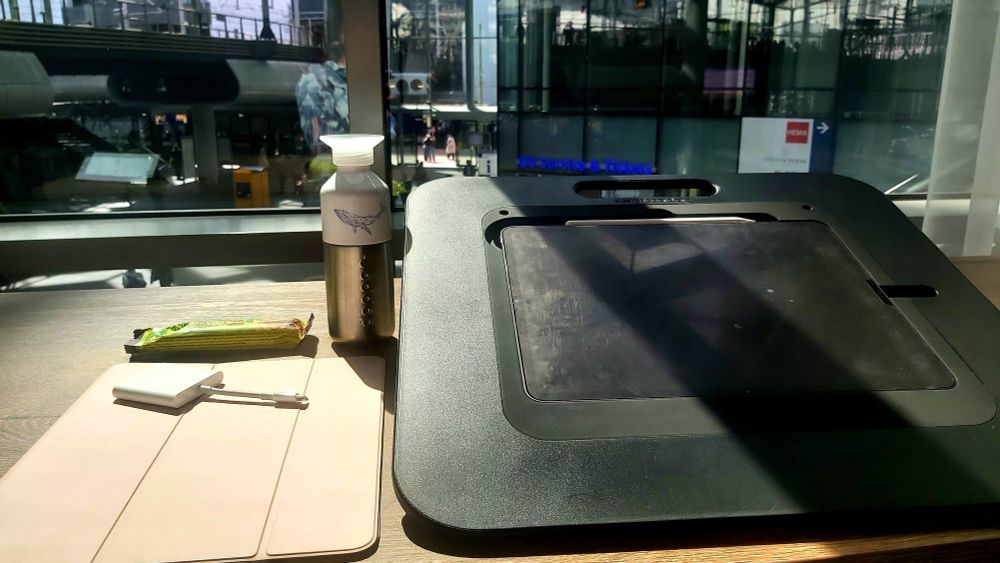 tafel met ipad, waterfles en snack met uitzicht op station Den Haag Centraal.