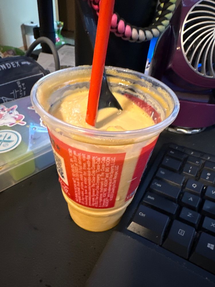 a photo of a pumpkin pie spice frosty from wendys, with a straw and a spoon in it, sitting on a desk