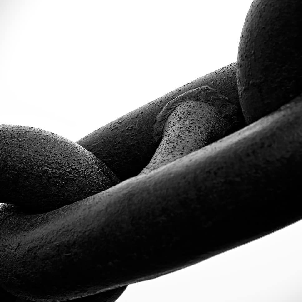Picture of dark and wet link of an anchor chain in front of a bright background. 
