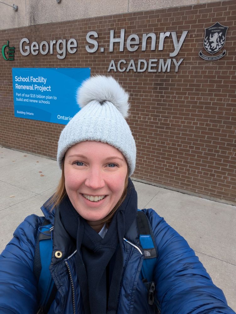 A smiling Dr. porteus standing in front of a red brick building, her old highschool 