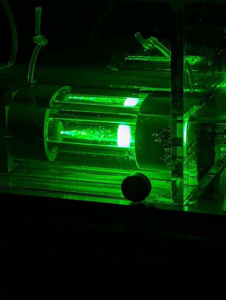 A picture of a swim tunnel in the dark with a green laser shining through it. The chamber contains fluorescent beads used to calibrate the water velocity 
