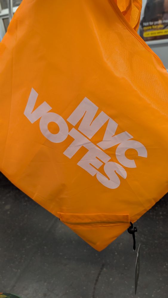 Bright orange NYC votes tote bag he'd up on the subway. It has a drawstring so that it can be folded up and the handles (not visible) are long enough to go over your shoulder and are attached so the bag will lay flat against your body, ie. The "right" way bag handles should go.