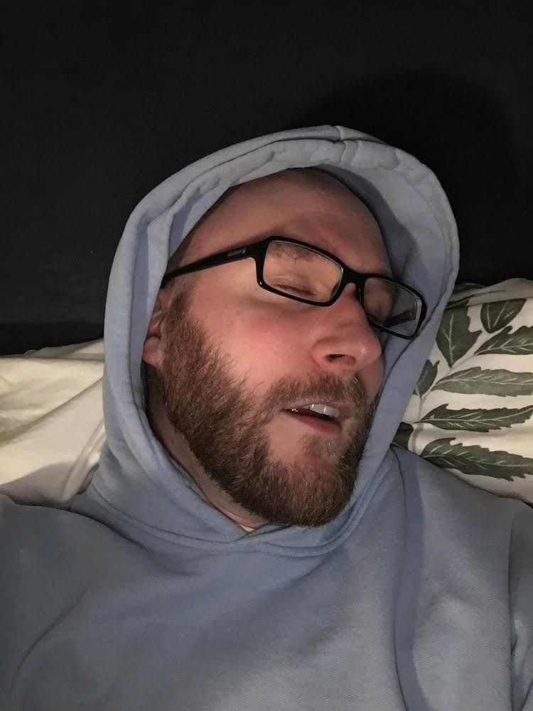 a bearded man with glasses lying in repose, overwhelmed by emotion