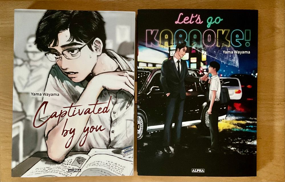 Two covers of books by Yama Wayama : the left one is "Captivated by you" with a teenage boy in class, wearing glasses and sweating, looking away. The right one title is "Let’s go karaoke !" with a middle aged man in a suit who hands an umbrella to a teenager under the rain. There is a city in background who light up the street with parked cars.