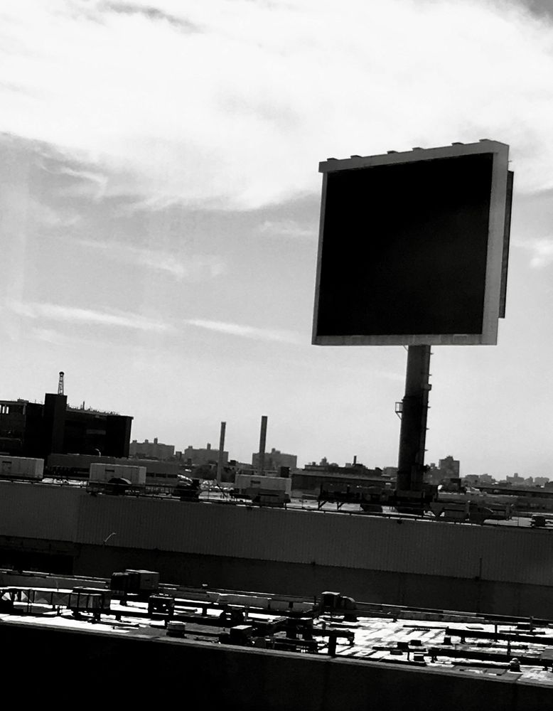 view from bus headed to nyc: urban skyline including smokestacks, rooftop utilities and giant unlit unfunded billboard