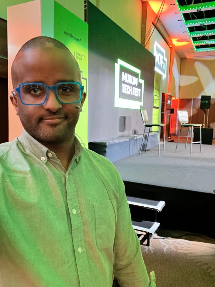 Selfie of Ahmed who is smiling, mic'd up and standing in front of the Muslim Tech Fest stage.