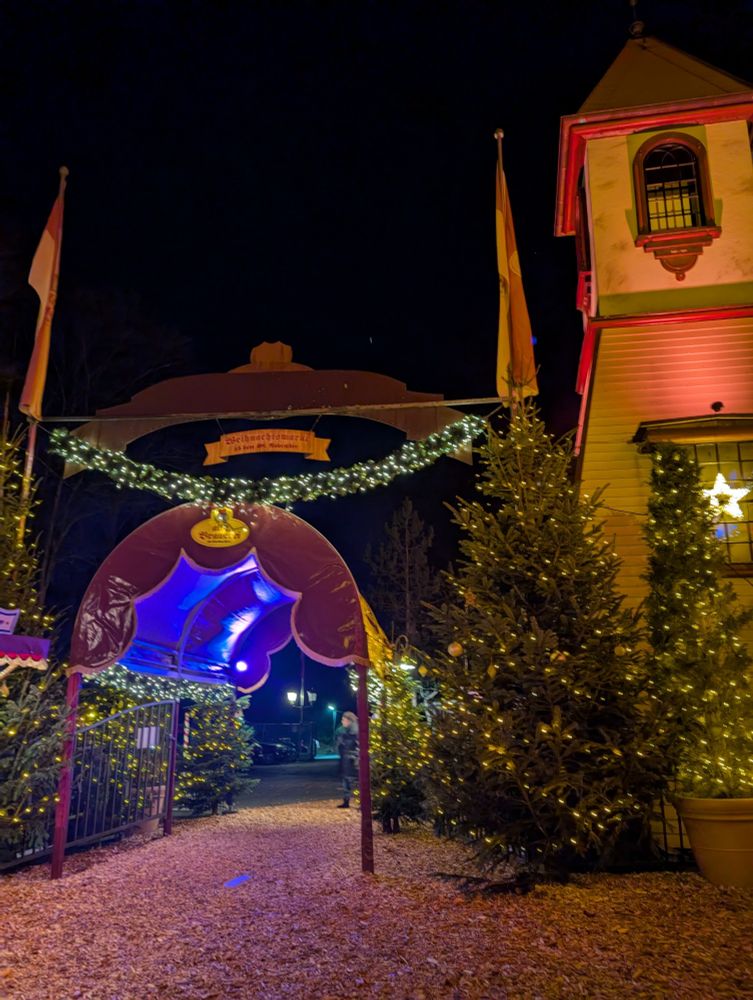 Ausgang vom Weihnachtsmarkt mit Türmchen, Weihnachtsbaum und Lichterketten.