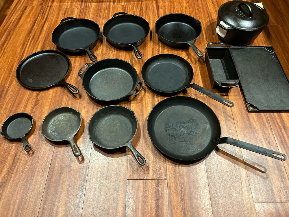 Various pieces of cast iron cookware and 2 carbon steel skillets spread out on the floor