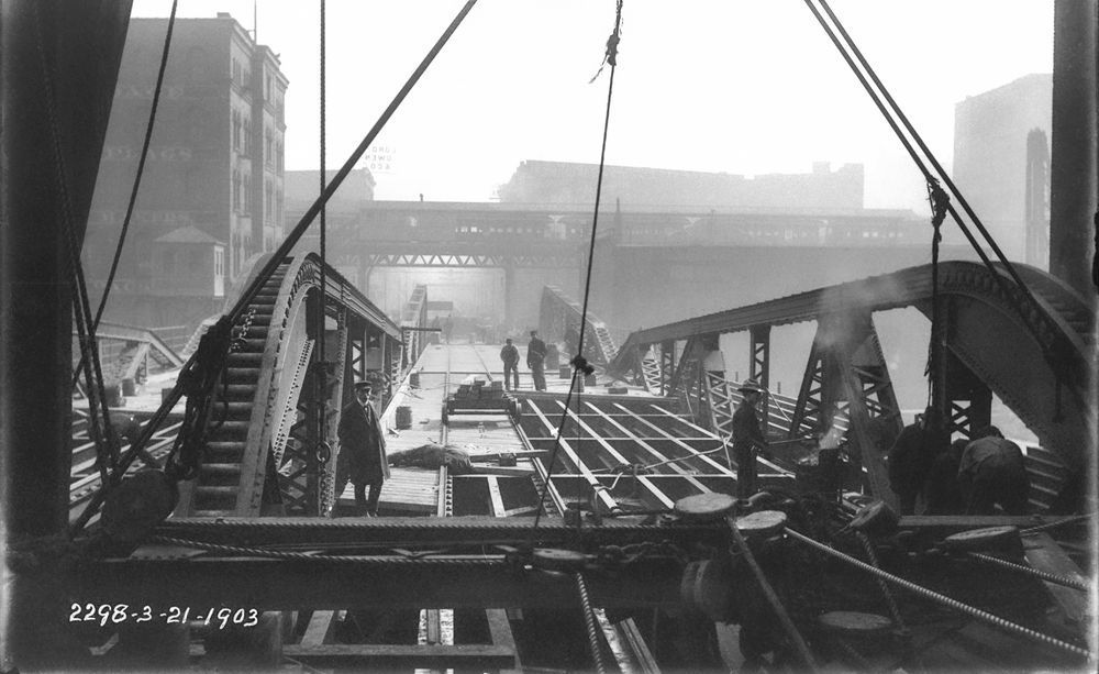 Construction of a bridge at Randolph Street and the South Branch of the Chicago River, viewed looking east, on March 21, 1903. Workers are seen in the foreground and an elevated commuter train is seen in the background. Learn about the work of the MWRD on our YouTube channel: https://youtu.be/__yXMrBYek4


