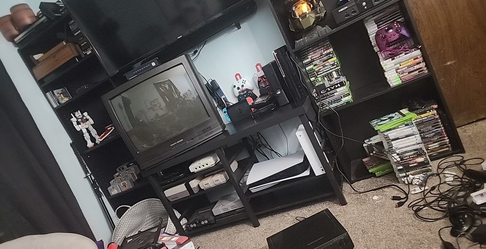 A collection of video game consoles and video games, surrounded by a mess of wires while I try to manage the cables and make my game room look nice.