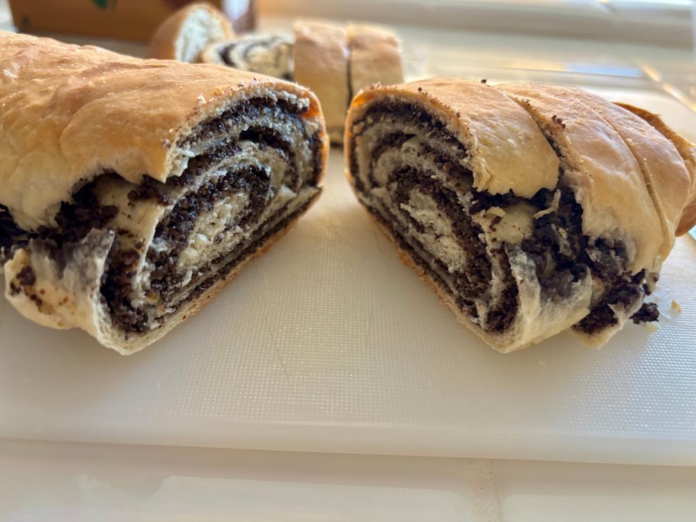 Image of a makowiec cake cut in half with light colored pastry and a swirl of dark poppyseed filling. 
