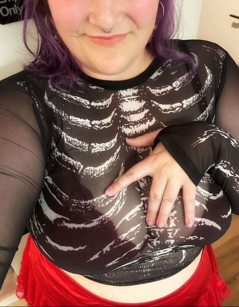 Photo of a curvy body in a little red skirt and a little cropped sheer skeleton shirt, a red lacy bra