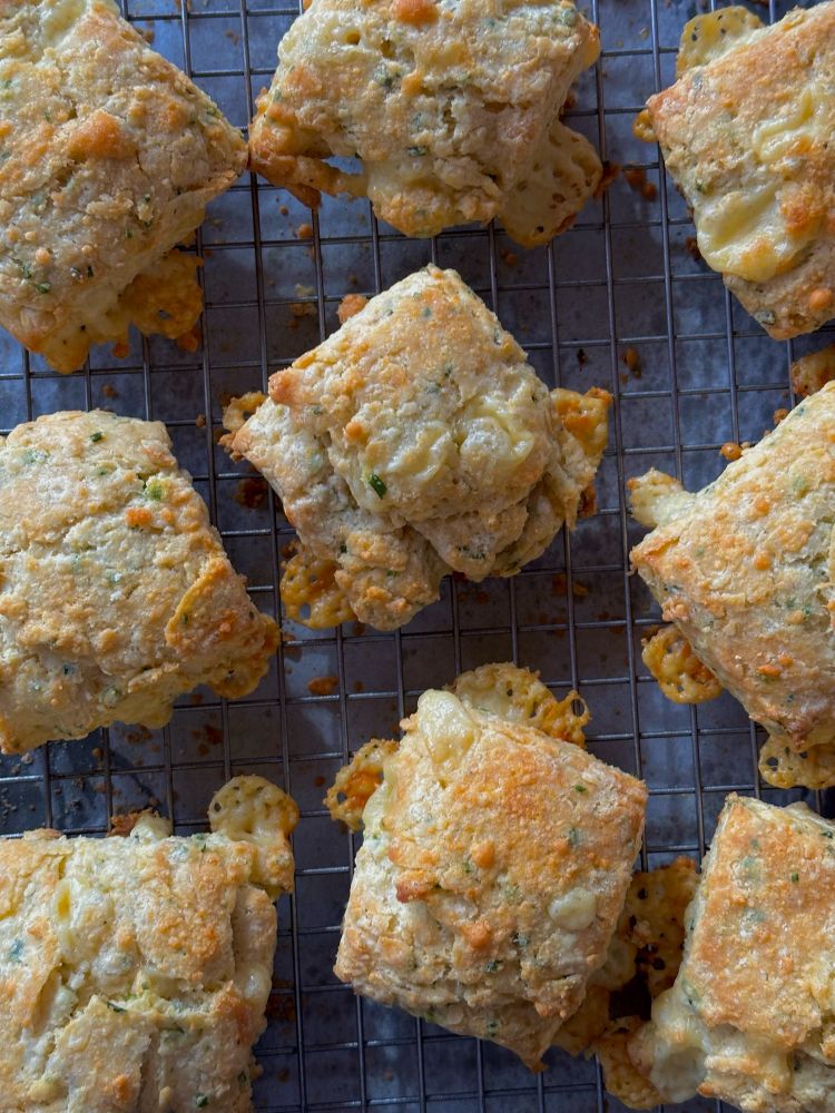 Cheddar and chive scones on a cooling rack with crispy cheese on the edges. Delicious!