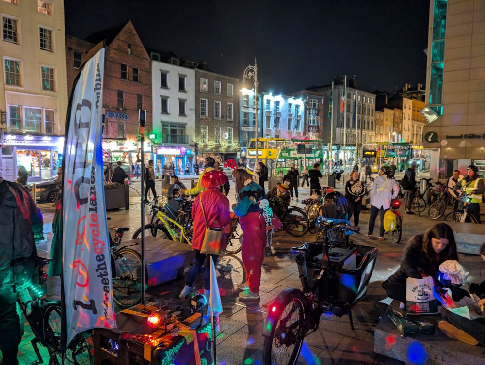 Crowd of people with bicycles in a square at night. There is a party atmosphere.