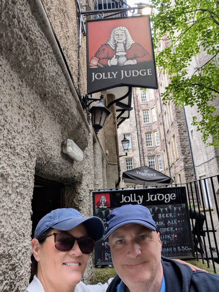 A couple pose in front of a pub sign that reads Jolly Judge.