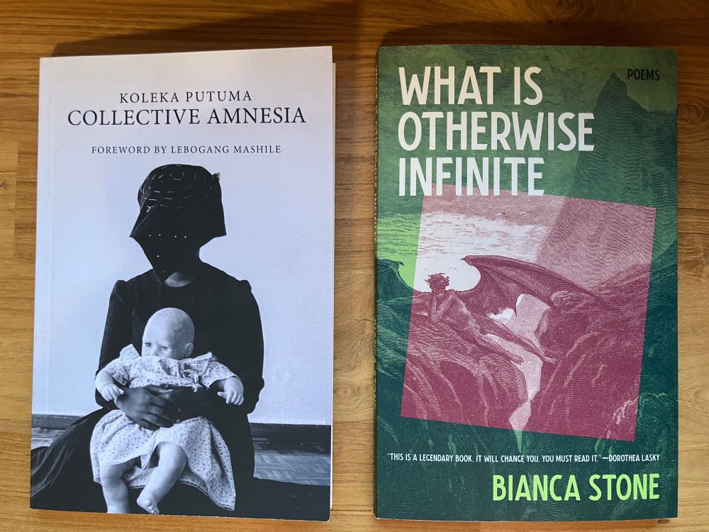 Two books sitting on a wooden table: Keleka Putuma's Collective Amnesia, whose cover shows a person in an elaborate face covering and a dark dress holding an infant in a light-colored dress, and Bianca Stone's What is Otherwise Infinite with a green overlay on an originally sepia-toned painting of a demon leaning across two rocks with the sea in the background. 