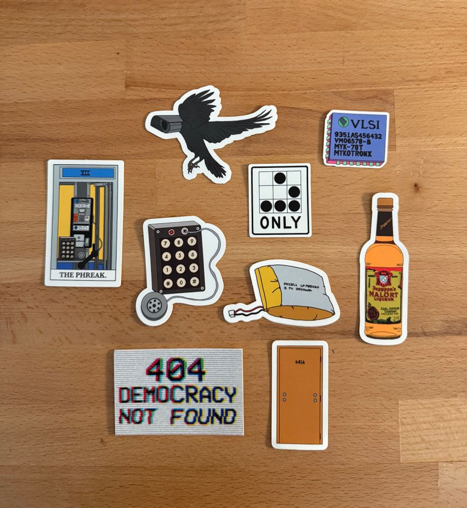 Image depicts a variety of stickers: a malort bottle, 404 democracy not found, a blue box, a tarot card, a bird with a camera for its head, the Clipper chip, and a spicy pillow. 