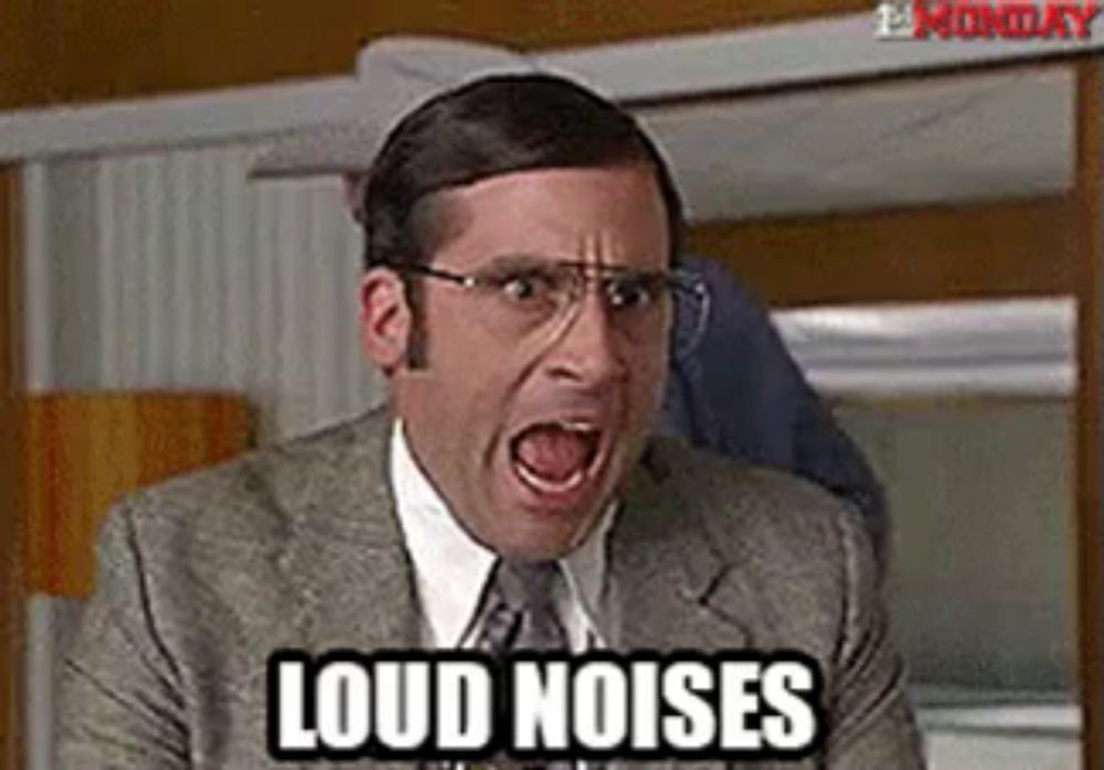 a man in a suit and tie is screaming with his mouth open and the words `` loud noises '' written on his face .