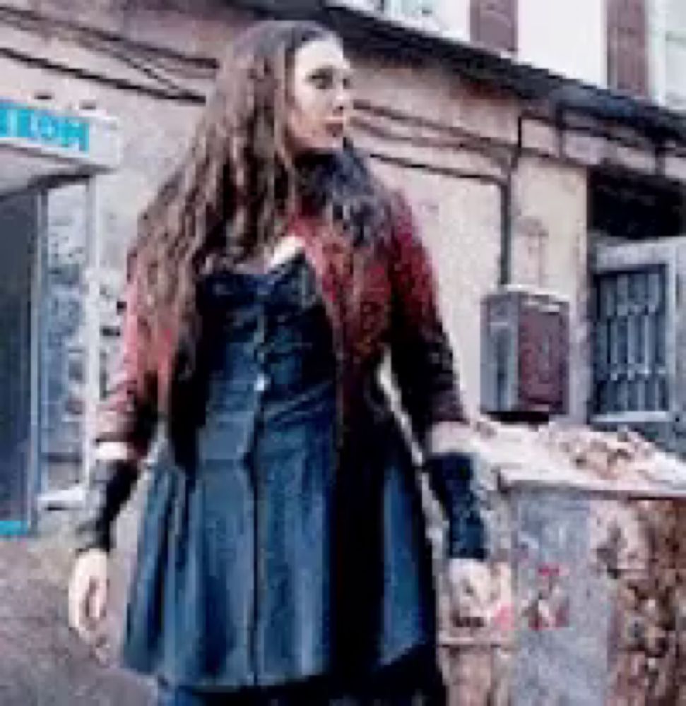 a woman in a blue dress and red jacket is standing in front of a trash can .