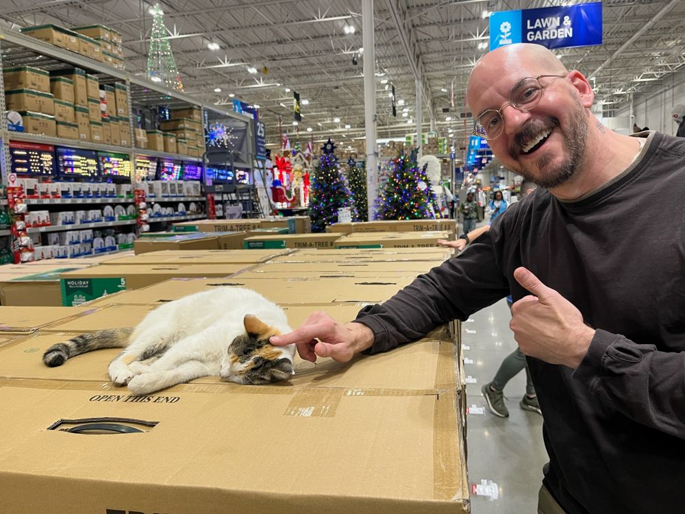 Bald guy in glasses smiling and giving thumbs-up next to sleeping Francine, the Lowes cat that worried a small city when she went missing