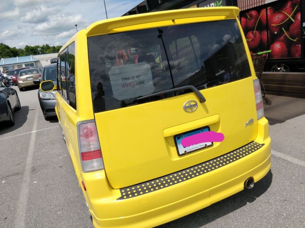 A photo of a yellow scion xB, with a sign in the back window 