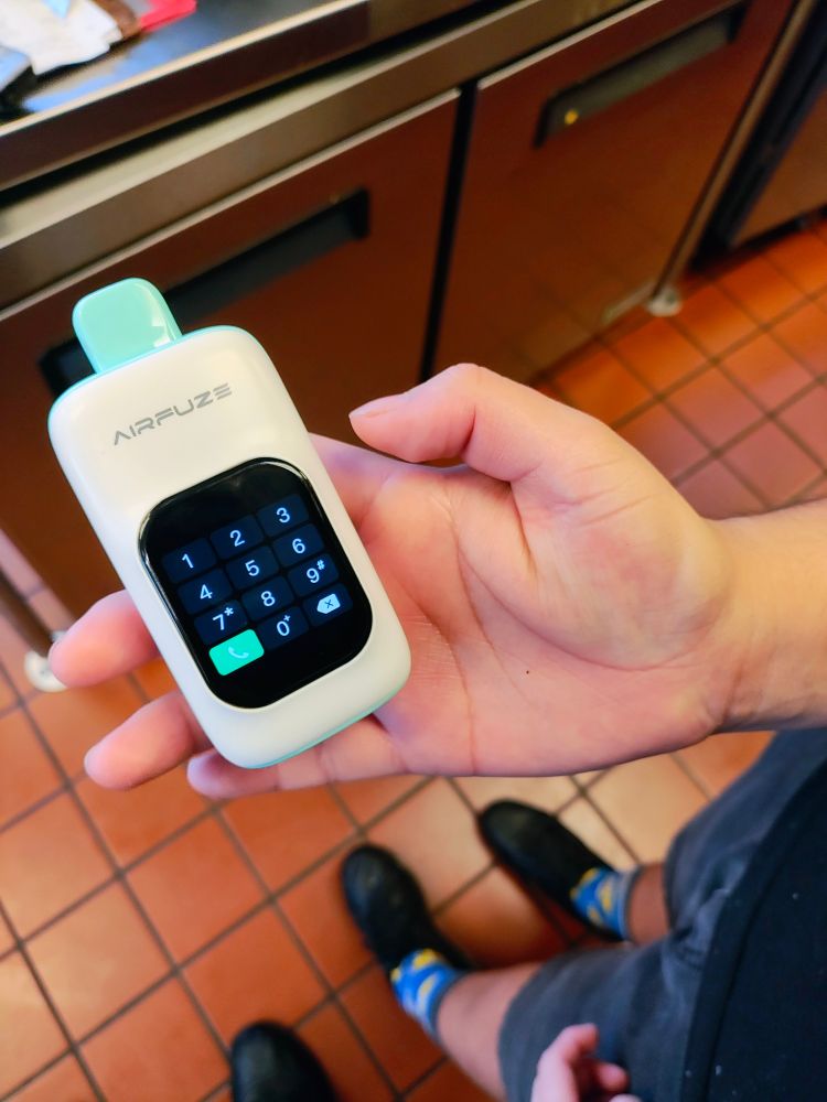 close-up of a person holding a vape stick that for some reason has a screen built-in and can make phone calls