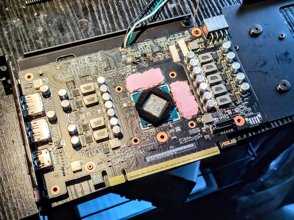 Asus Prime Radeon 9060XT PCB with heatsink removed. Pink thermal putty has been added to the VRAM, and liquid metal is applied to the core with a foam safety barrier to keep the liquid metal contained. Two tiny enameled copper wires are soldered to the board for messing with Power Limit, and a cable has been added to the i2c header for attaching to Elmor EVC2 to control voltage