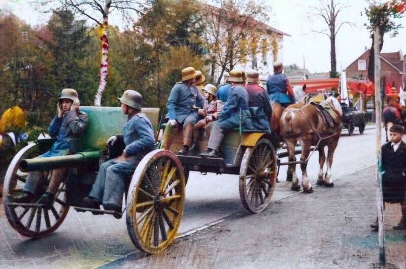 Nachträglich coloriertes Bild eines Pferdegespannes aus Weltkriegszeiten (mutmaßlich WK1)  mit angehängter gezogener Kanone eines mir unbekannten Typs. Mehrere Soldaten sitzen auf dem Gespann und der gezogenen Kanone. Szene im städtischen Umfeld, gepflasterte Straßen, zwei Häuser im Hintergrund. Ein Junge schaut zu, weitere Pferde voraus zu sehen. 