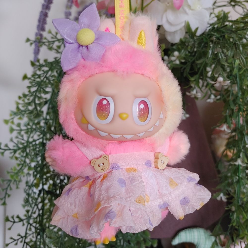 Loyalty labubu wearing a pink dress and a flower hair accessory in front of fake plants 