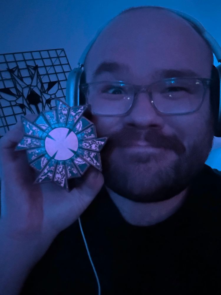 Selfie in a dimly blue-lit room while holding a solved Lament Configuration