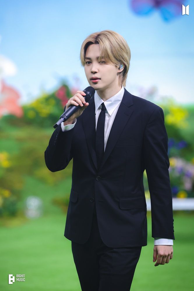 Jimin wearing a suit and holding a microphone on the set of the Smeraldo Garden Marching Band music video.