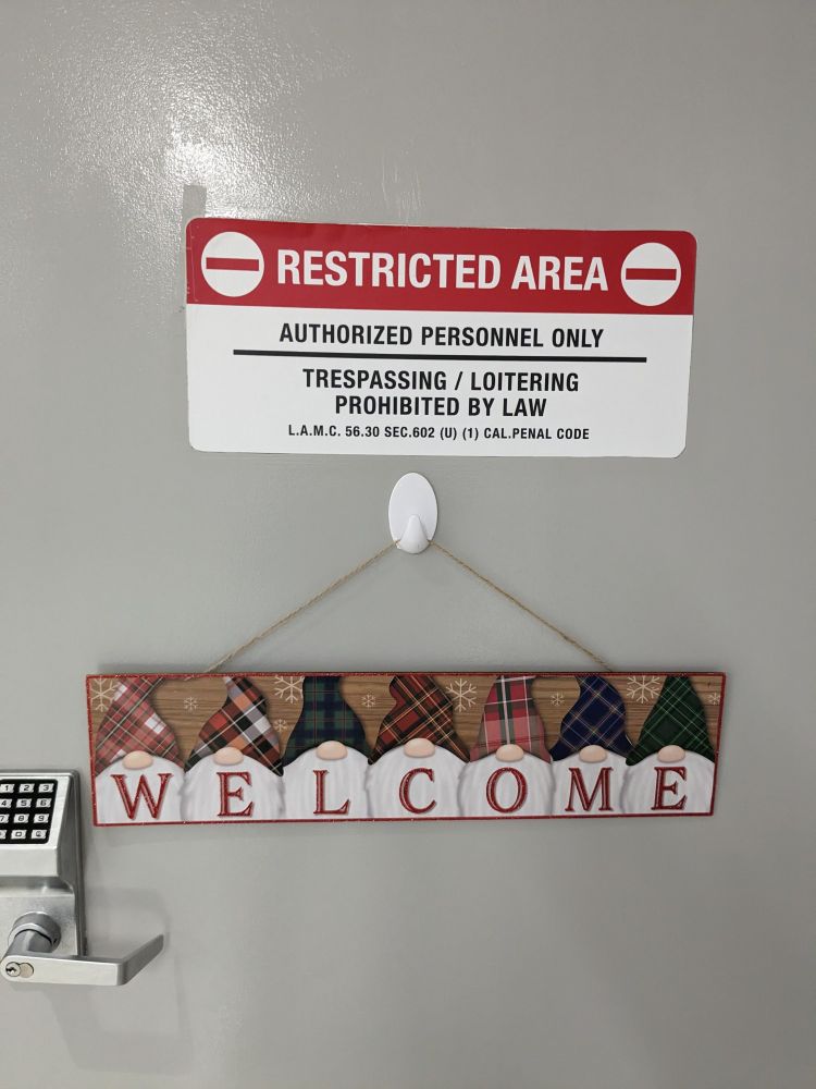 A forbidding "Restricted Area" sign with a festive "Welcome" sign hanging below