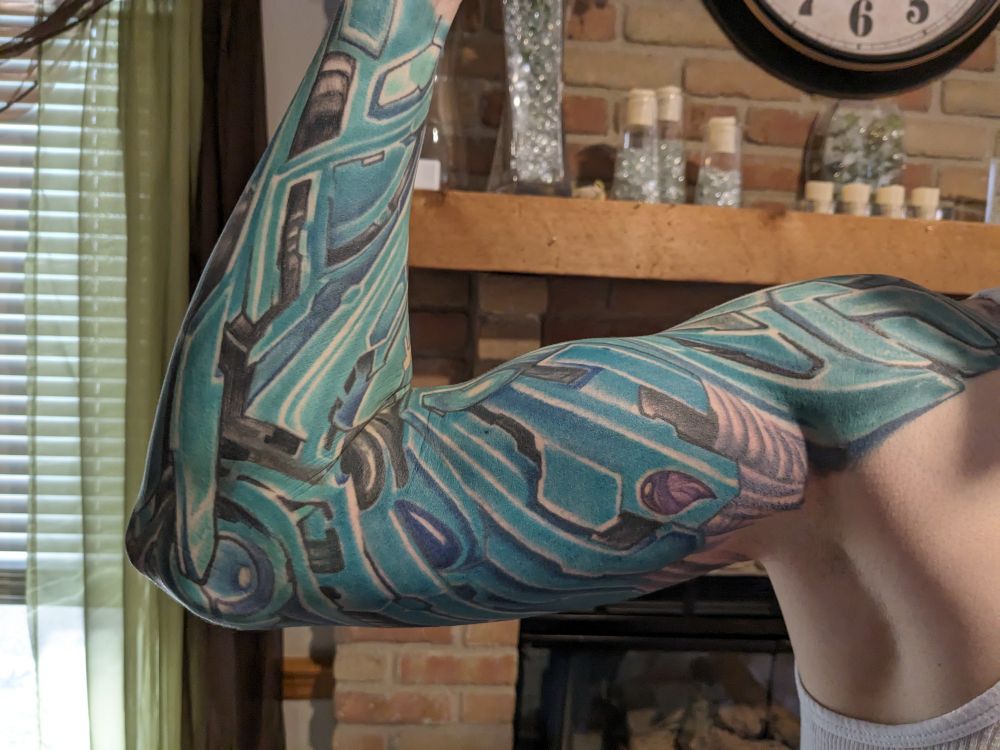 A view of a man's arm showing his blue mechanical arm sleeve tattoo. He's flexing his bicep.