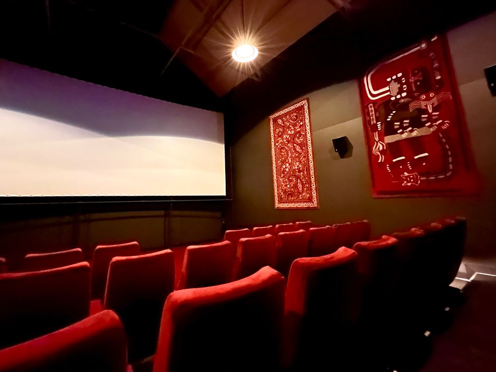 Inside of the cinema. Plush seating in rows, large canvas at the front. Movie has not started yet.