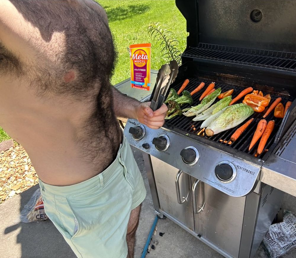 shirtless hairy man at grill with romaine, several carrots, broccoli, and bell peppers and metamucil container
