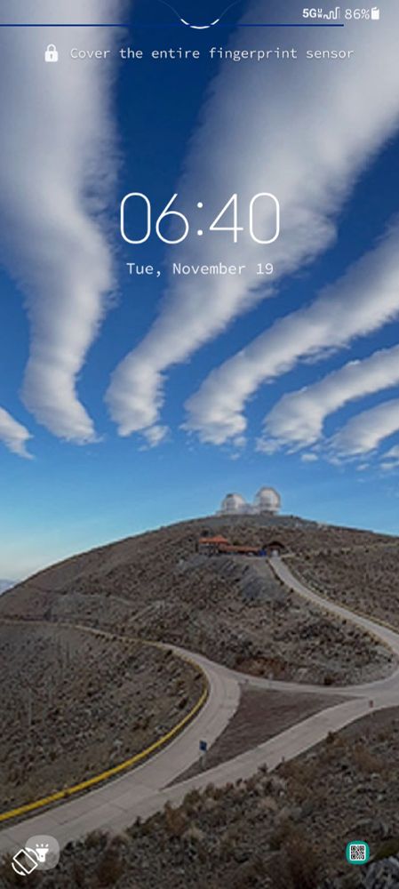 Picture of a lock screen, hills without grass on them in the background, buildings further up the hill, roads on the hills.