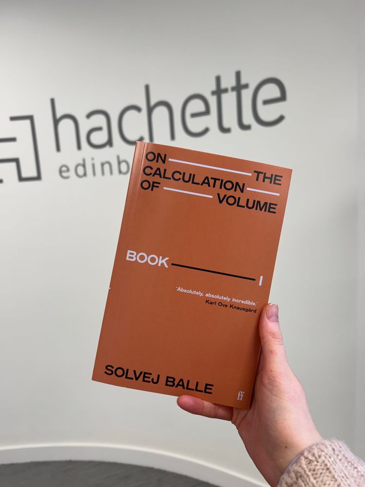 my hand is holding a proof copy of Solvej Balle’s On the Calculation of Volume. the wall in the background has printing on it saying Hachette Edinburgh 