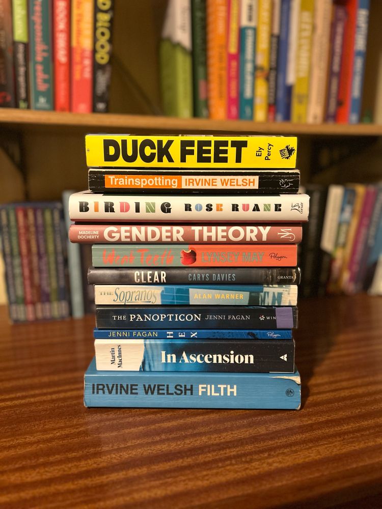 A stack of books: Irvine Welsh’s Filth, Martin MacInnes’ In Ascension, Jenni Fagan’s Hex and The Panopticon, Alan Warner’s The Sopranos, Carys Davies’ Clear, Lynsey May’s Weak Teeth, Madeline Docherty’s Gender Theory, Rose Ruane’s Birding, Irvine Welsh’s Trainspotting, Ely Percy’s Duck Feet