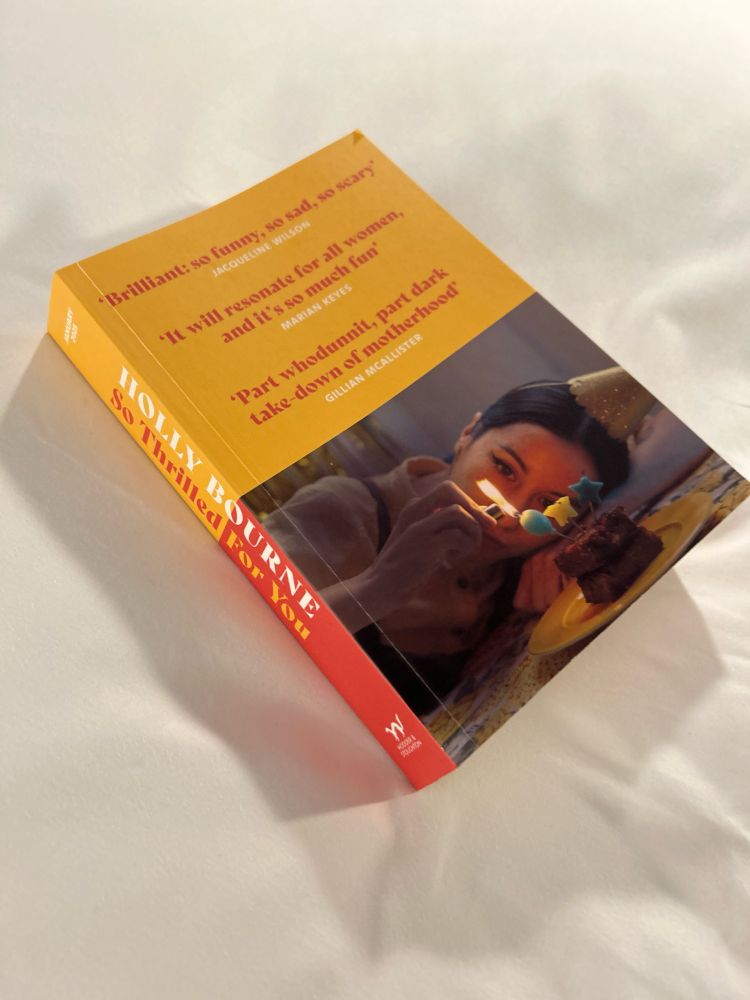 a copy of Holly Bourne’s So Thrilled for You lies on a bedsheet