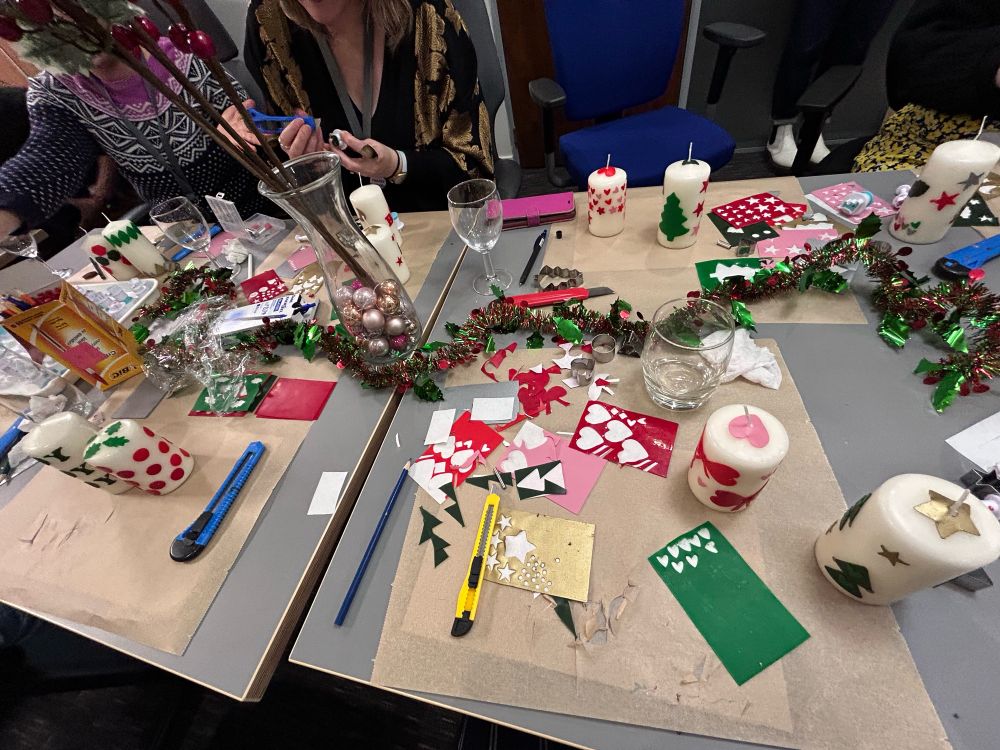 a table covered in crafting materials and candles which are being decorated. tinsel and other christmas ornaments adorn the table 