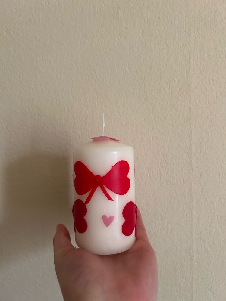 the user’s hand is holding a thick white candle decorated with red bows and pink hearts