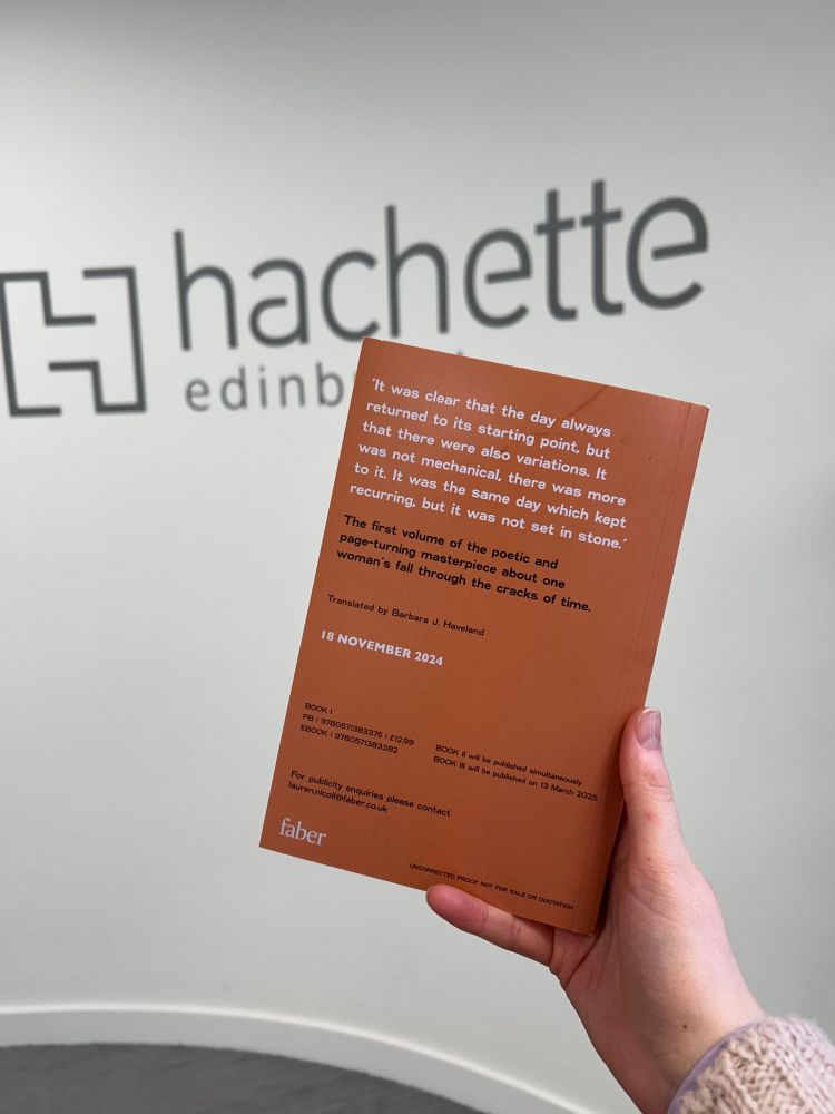 my hand is holding a proof copy of Solvej Balle’s On the Calculation of Volume. the wall in the background has printing on it saying Hachette Edinburgh 